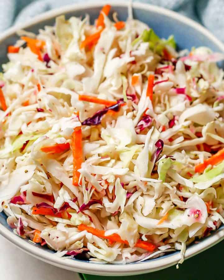 Close up of no mayo coleslaw in a blue and white bowl with colorful napkins nearby.