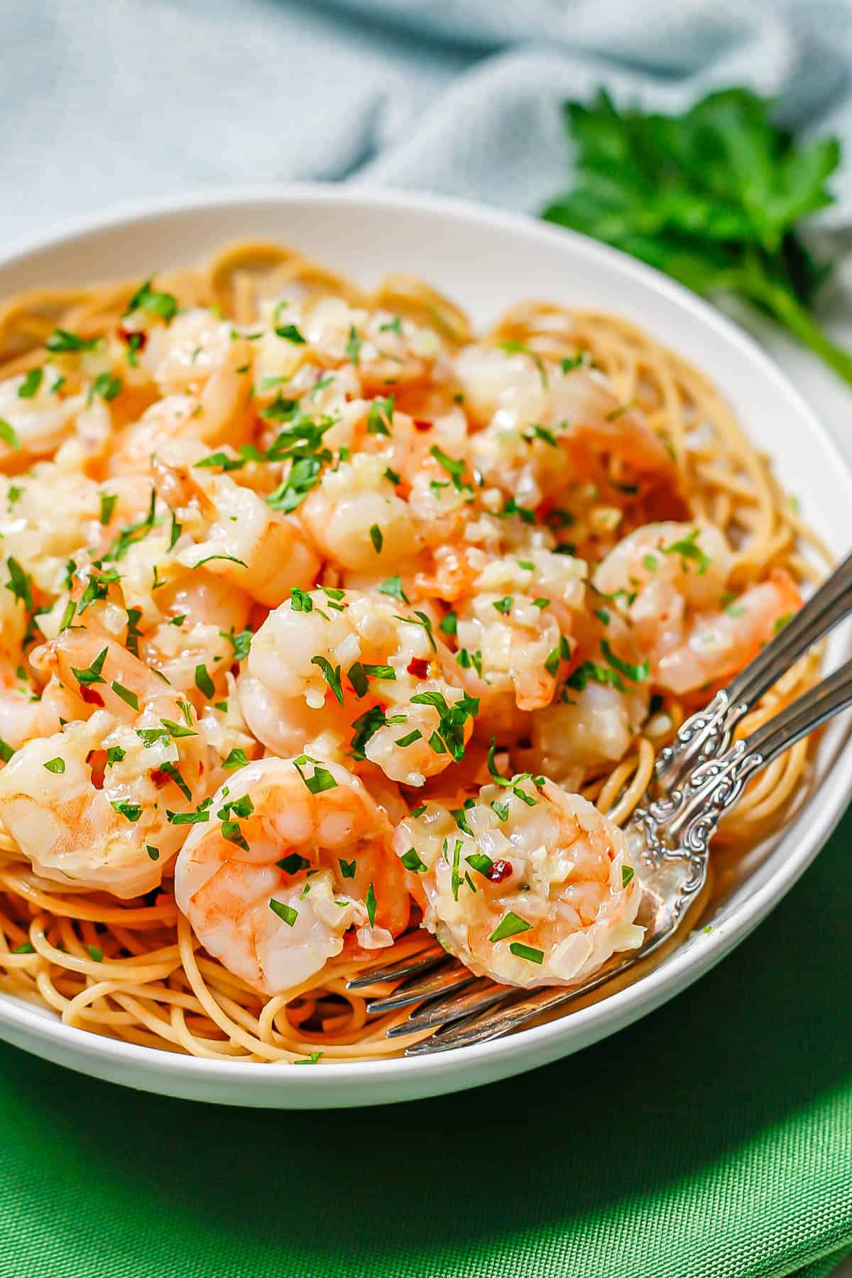 Two forks resting in a white bowl filled with pasta topped with shrimp in a butter sauce.