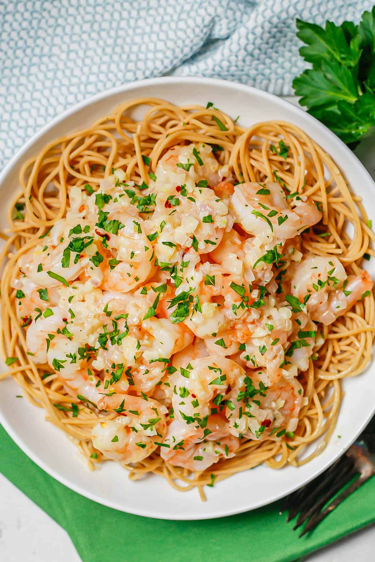 A low white bowl with spaghetti topped with garlic butter shrimp and sprinkled with parsley.