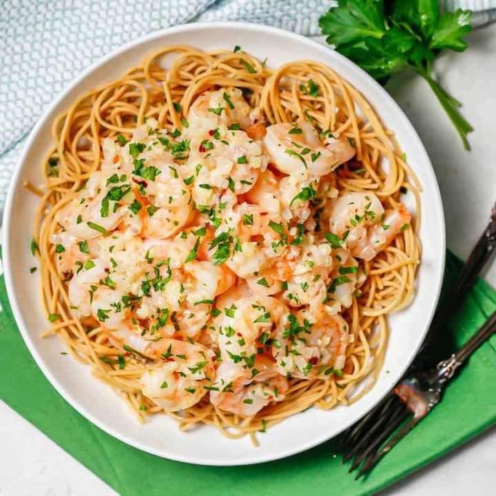 A low white bowl with spaghetti topped with garlic butter shrimp and sprinkled with parsley with two forks to the side.