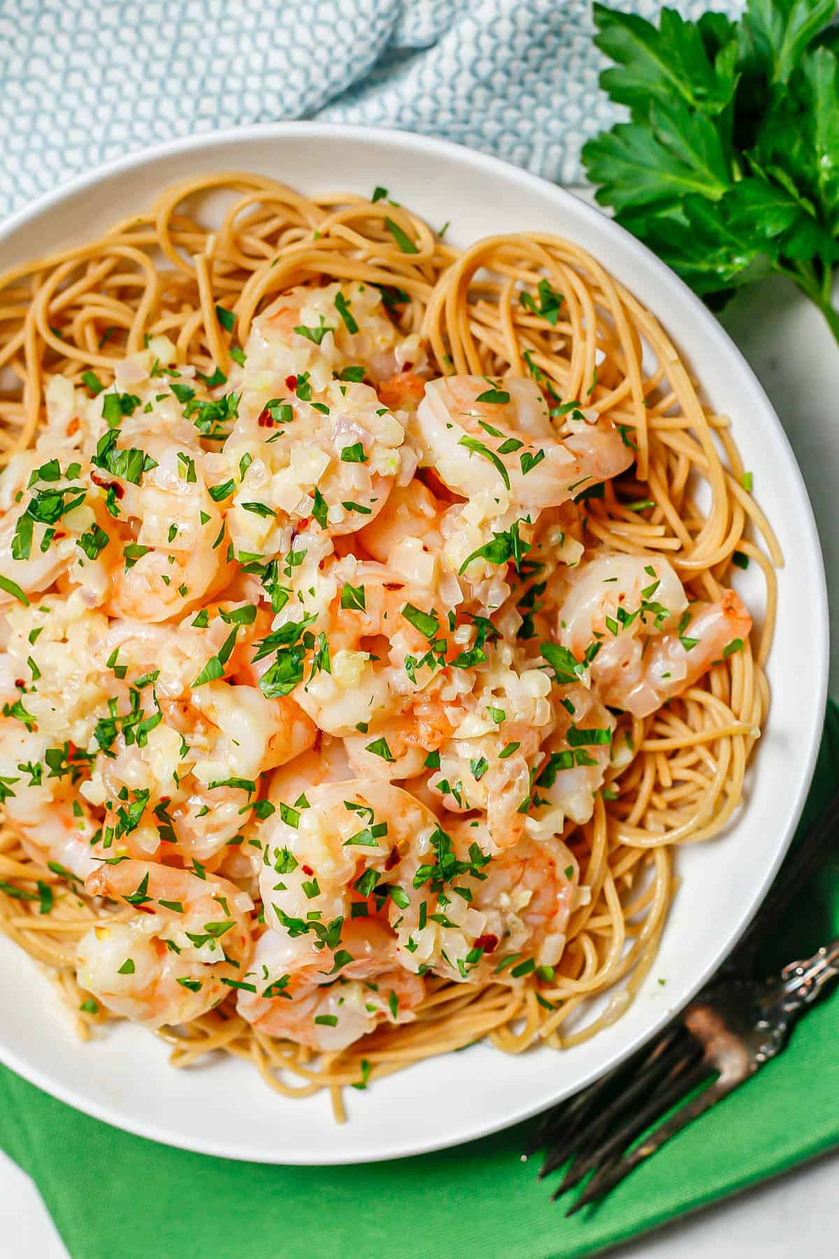 Garlic butter shrimp served over spaghetti noodles in a low white bowl.