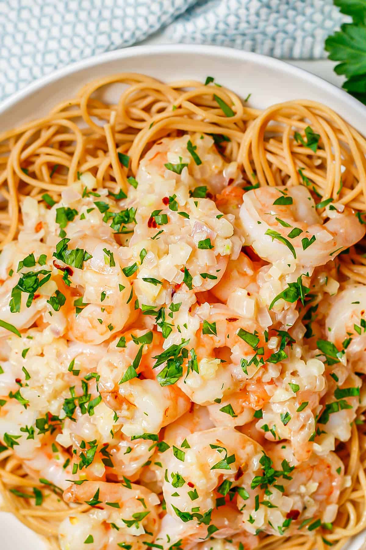 Close up of garlic butter shrimp over pasta in a low white bowl.