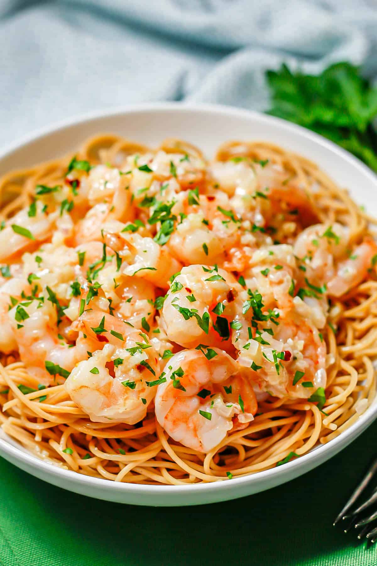 Shrimp in a shallot and garlic butter sauce served on top of spaghetti noodles in a low white bowl with parsley sprinkled on top.