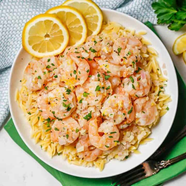 Shrimp served over top or orzo pasta with lemon slices and parsley to the side.