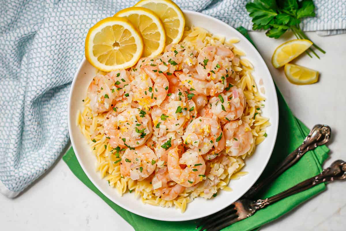 Shrimp served over top or orzo pasta with lemon slices and parsley to the side.