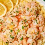 Lemon garlic shrimp served over orzo pasta in a low white bowl with parsley on top and lemon slices to the side and a text overlay on the photo.