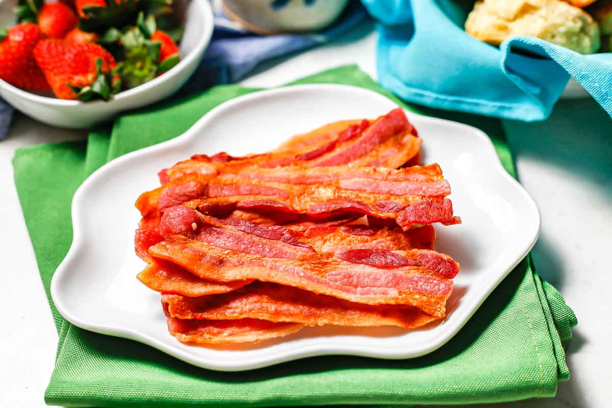 Microwave cooked bacon on a white plate with fluted edges set on green napkins.