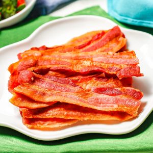 Close up of bacon on a white plate with fluted edges.