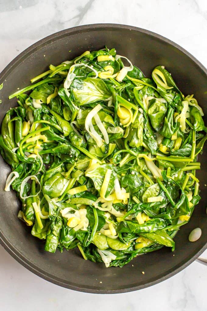 A mix of spinach and leeks being cooked in a large dark skillet.