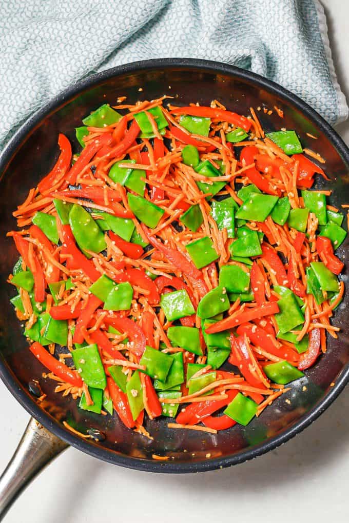 Red pepper, matchstick carrots and snow peas sautéed together in a pan.