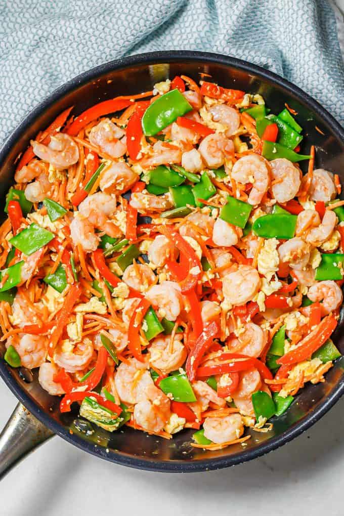 Shrimp and veggies and bits of cooked egg all mixed together in a large skillet.