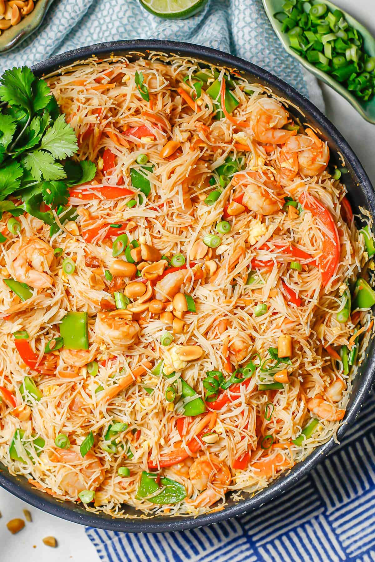 Close up of shrimp pad Thai with rice noodles and veggies in a large dark skillet.