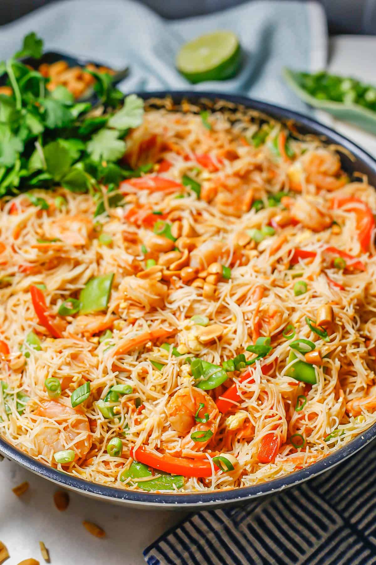 A large dark skillet with a shrimp and rice noodle mixture with veggies.