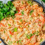 Shrimp pad Thai in a large skillet with peanuts and green onions on top and a bunch of fresh cilantro to the side and a text overlay on the photo.