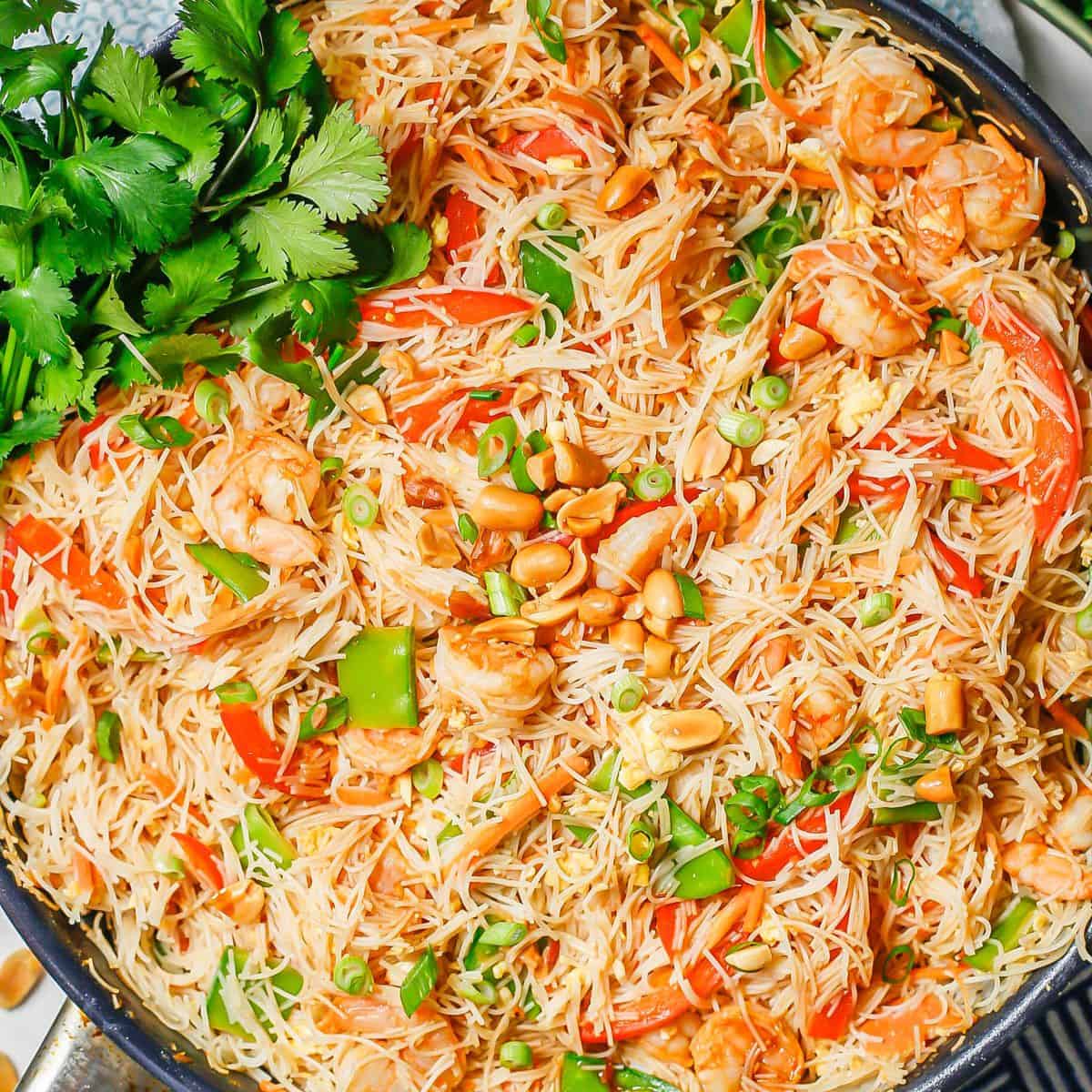 Close up of shrimp pad Thai in a large skillet with peanuts and green onions on top and a bunch of fresh cilantro to the side.