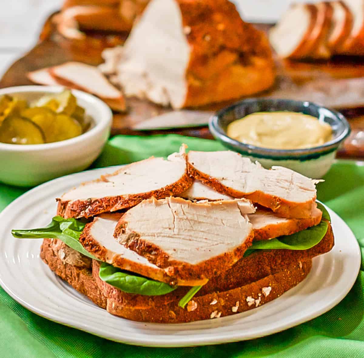 An open faced turkey sandwich on a white plate set on green napkins.