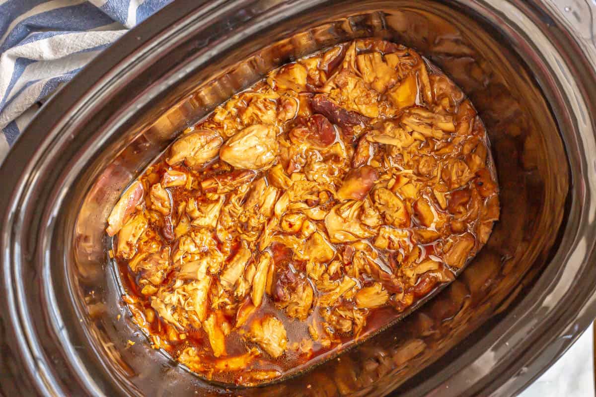 A slow cooker insert with cooked shredded chicken in an Asian honey garlic sauce.