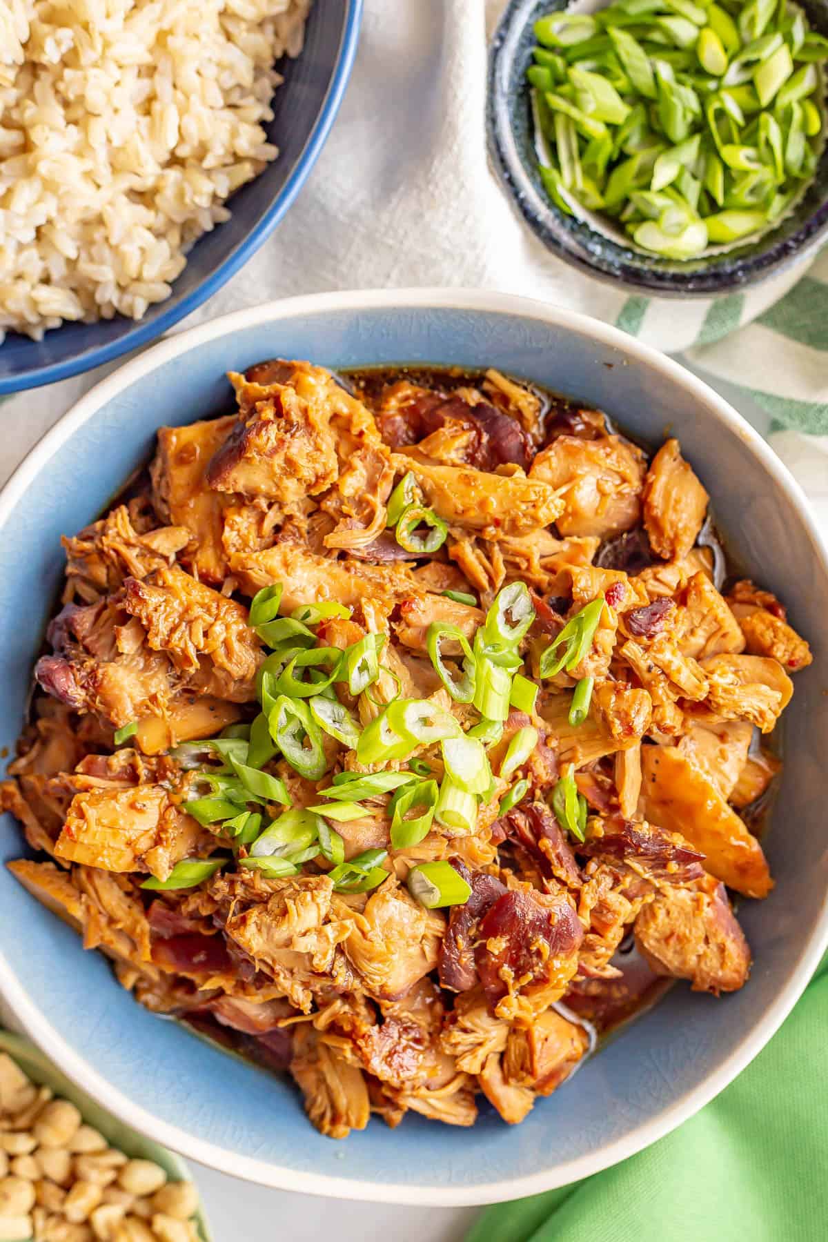 Honey garlic chicken served in a blue and white bowl with sliced green onions on top and to the side and a bowl of rice to the side.