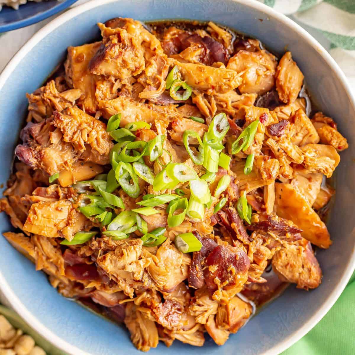 Close up of honey garlic chicken served in a blue and white bowl with sliced green onions on top.