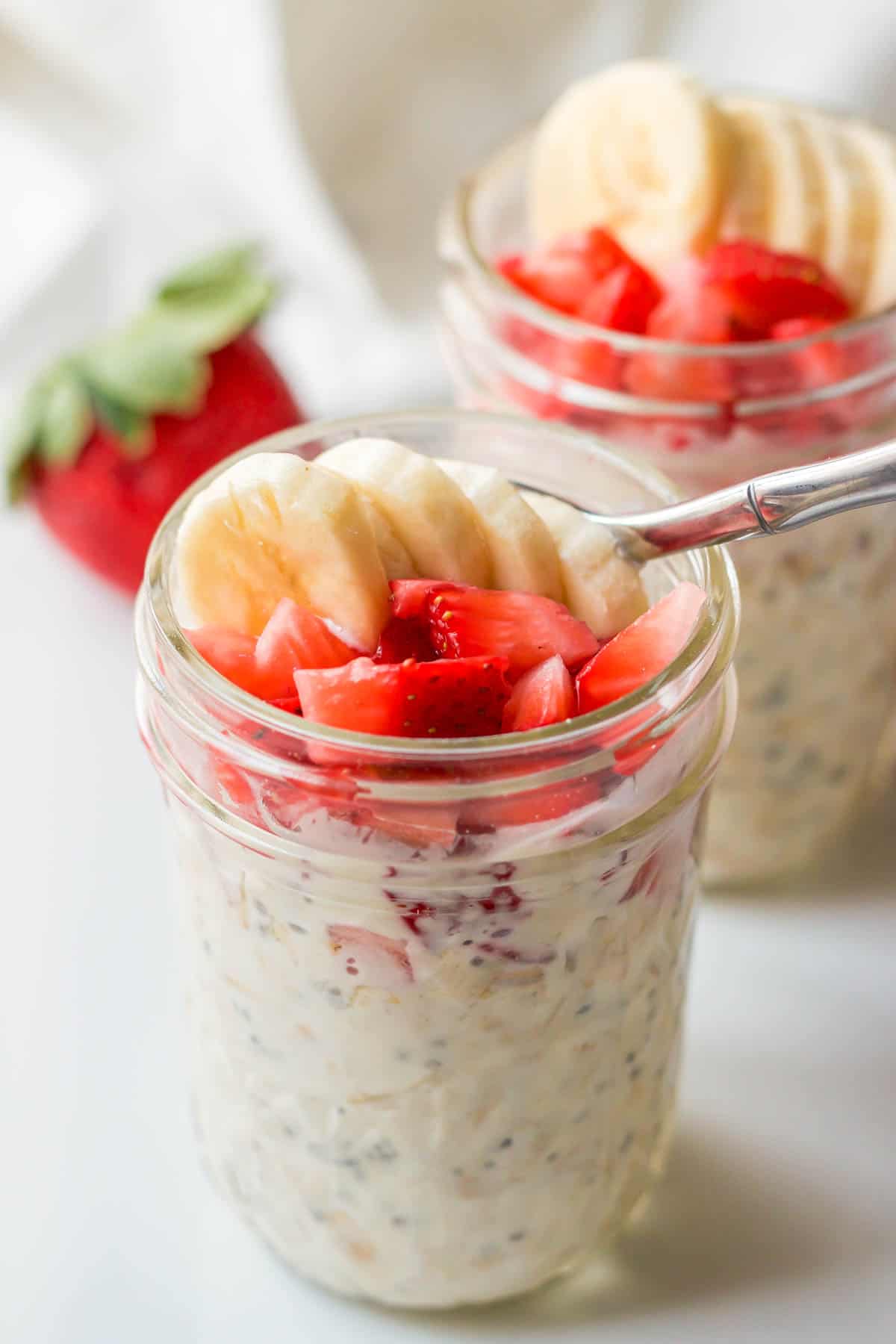 Close up of a strawberry banana overnight oatmeal jar with a spoon resting in the top.