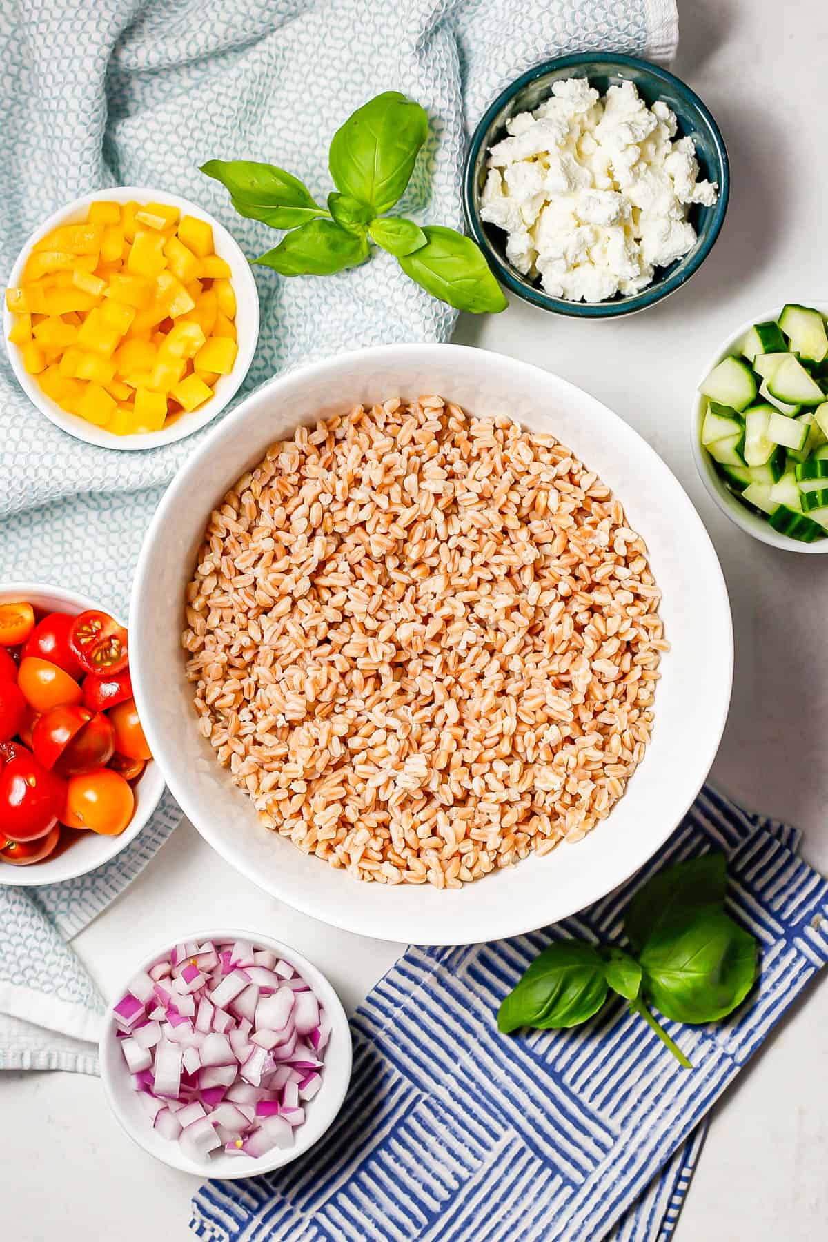 Ingredients laid out in separate bowls to make a summer farro salad with veggies and goat cheese.