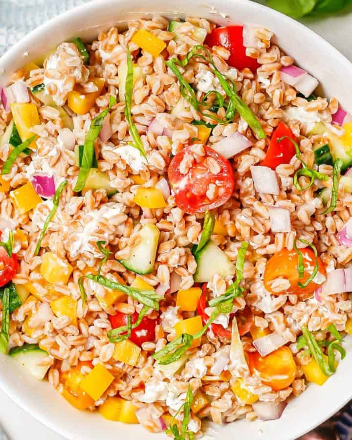 Close up of a bright, fresh summer farro salad with fresh veggies and basil in a white serving bowl.