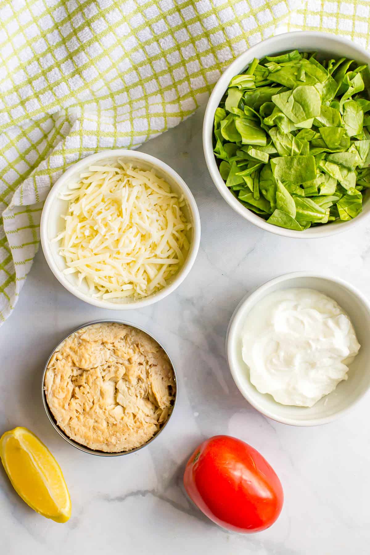 Ingredients laid out in different bowls on a white marble counter for making tuna spinach salad with tomatoes and mozzarella.