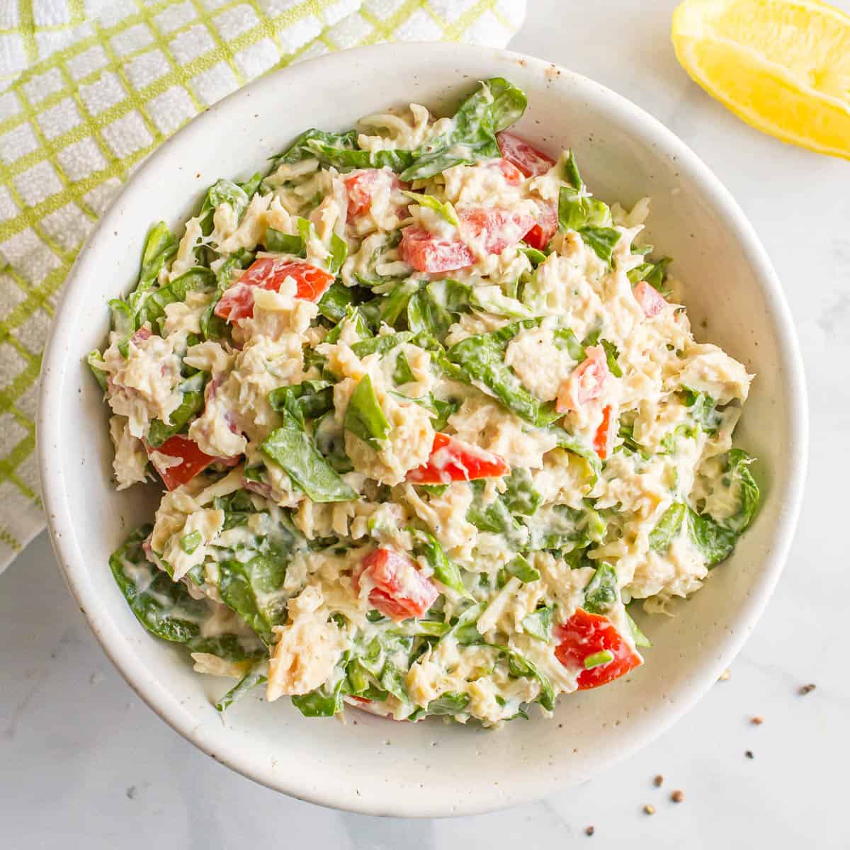 Close up of a creamy tuna spinach salad with tomatoes in a speckled white bowl.