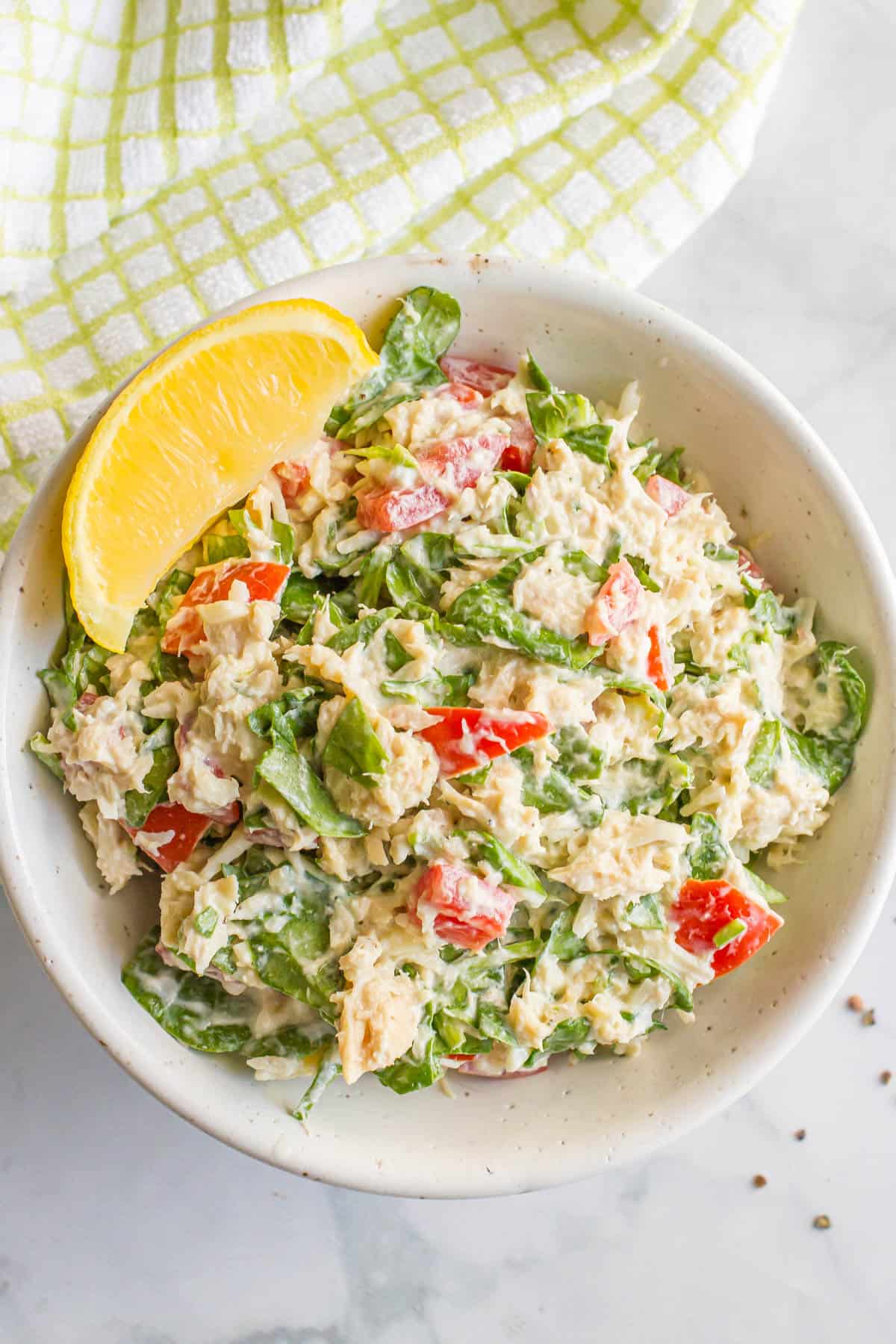 Tuna spinach salad with tomatoes in a speckled white bowl with a lemon wedge on the side.