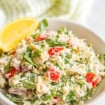 A healthy tuna spinach salad with tomatoes in a speckled white bowl with a text overlay on the photo.