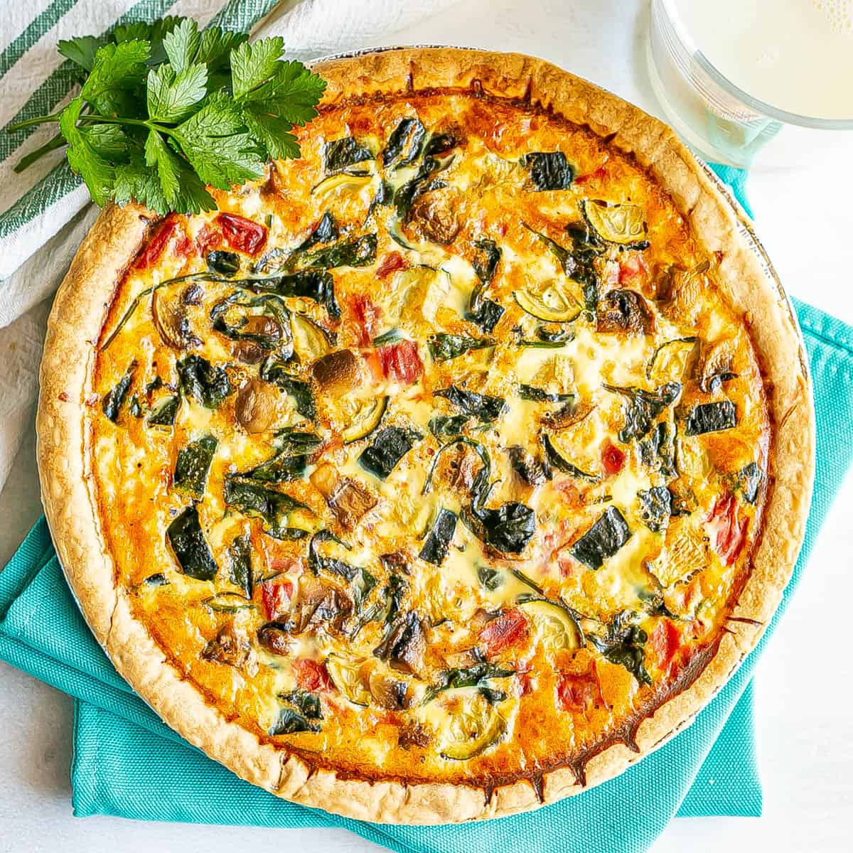 Close up of a veggie quiche set on teal napkins with a glass of milk to the side.