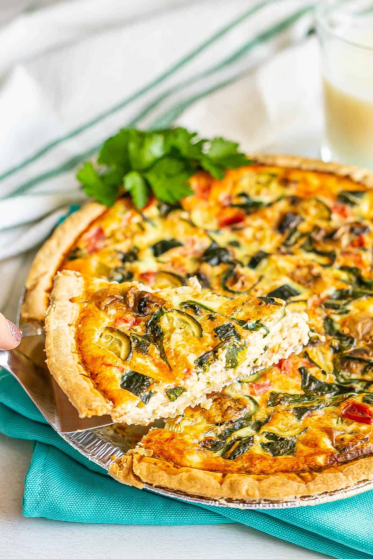 A piece of veggie lovers quiche being lifted out from the pie plate.