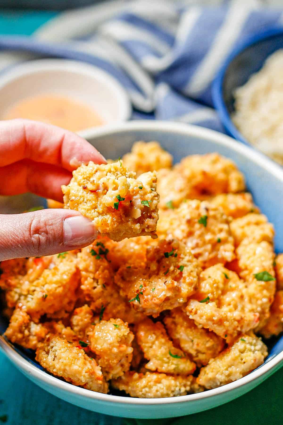 A hand holding up a piece of shrimp from a serving bowl.