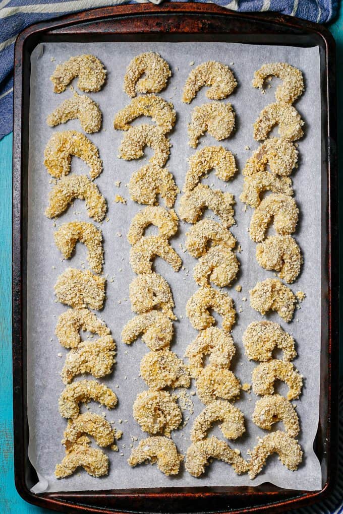 Breadcrumb crusted shrimp laid out on a parchment paper lined baking sheet before being cooked.