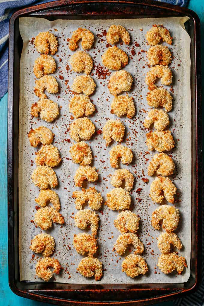 Baked breaded shrimp on a parchment paper lined baking sheet.