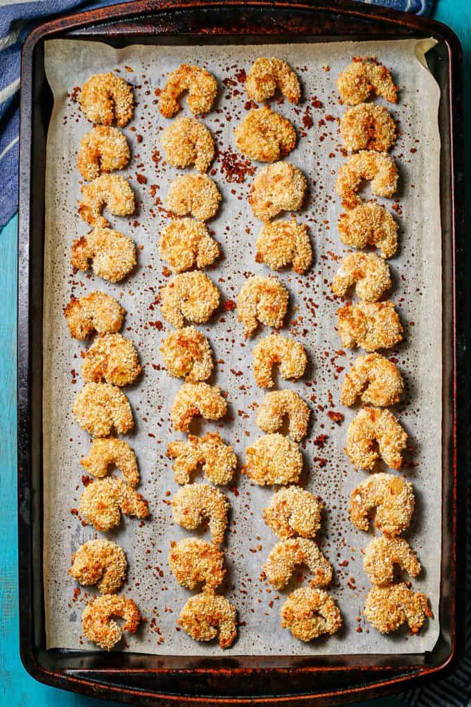 Baked breaded shrimp on a parchment paper lined baking sheet.