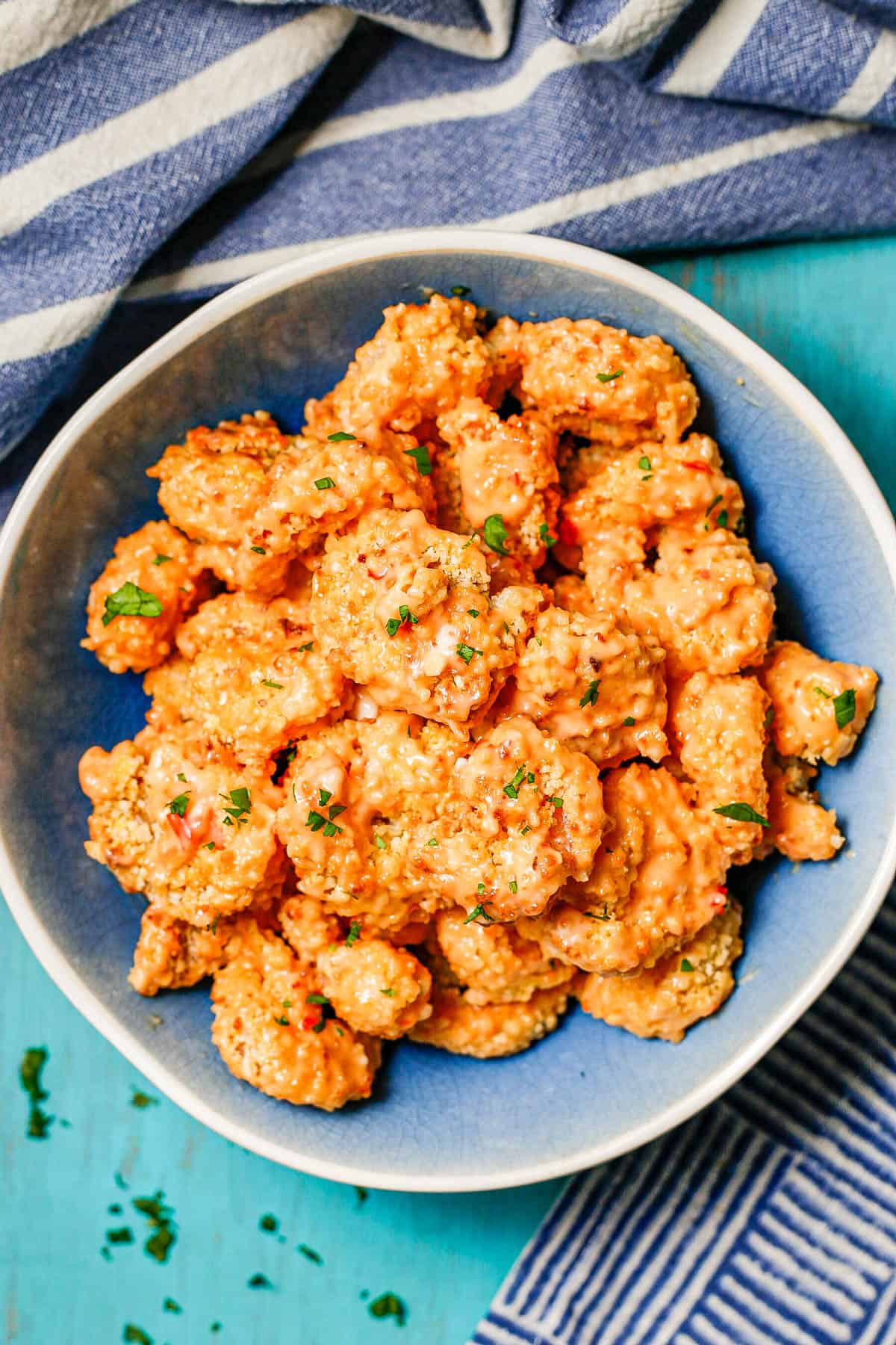 Bang bang shrimp served in a blue and white bowl with fresh herbs sprinkled on top.