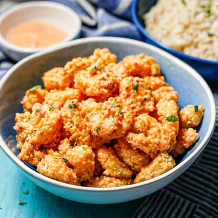 A bowl full of bang bang shrimp served alongside a bowl of steamed rice and a small bowl with extra sauce.