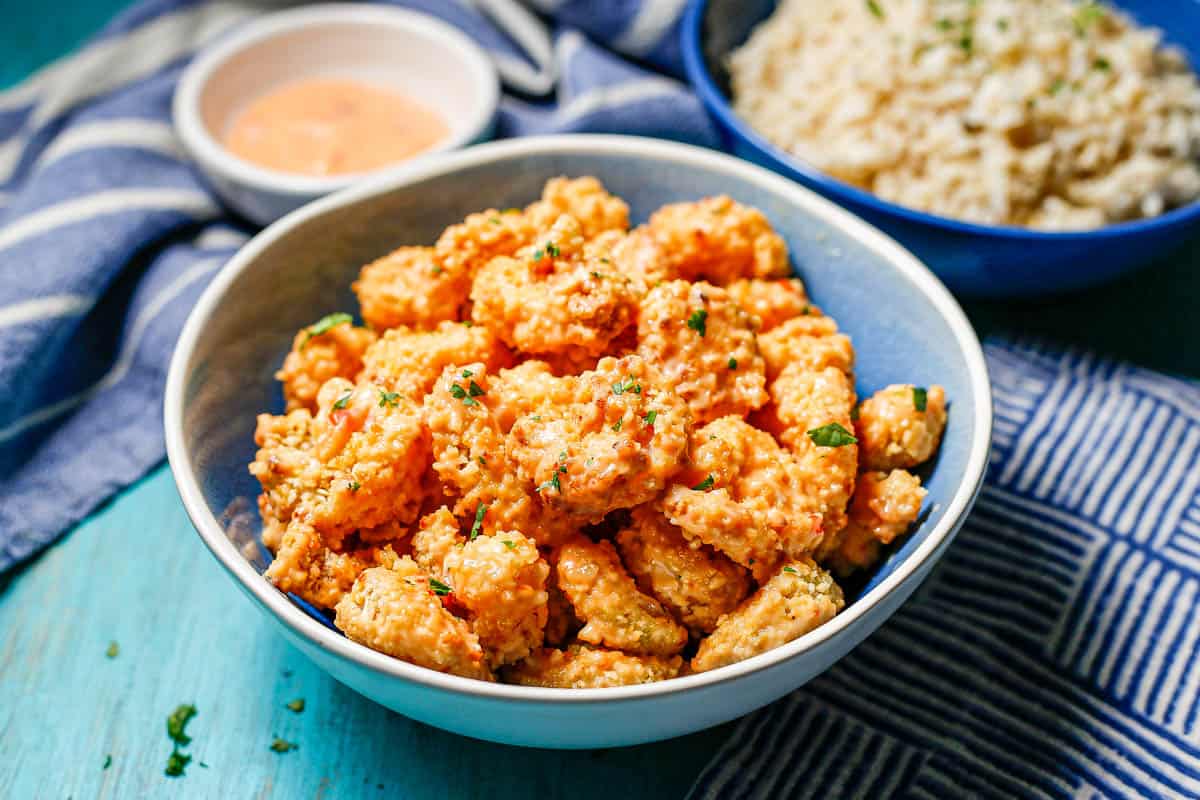 A bowl full of bang bang shrimp served alongside a bowl of steamed rice and a small bowl with extra sauce.