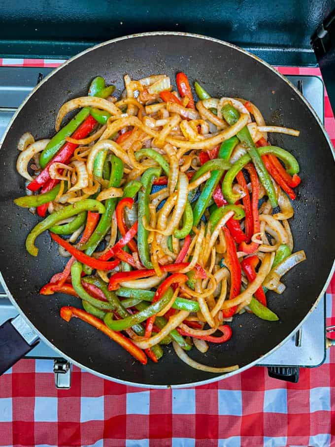 A large skillet with sautéed onions and peppers on a camp stove.