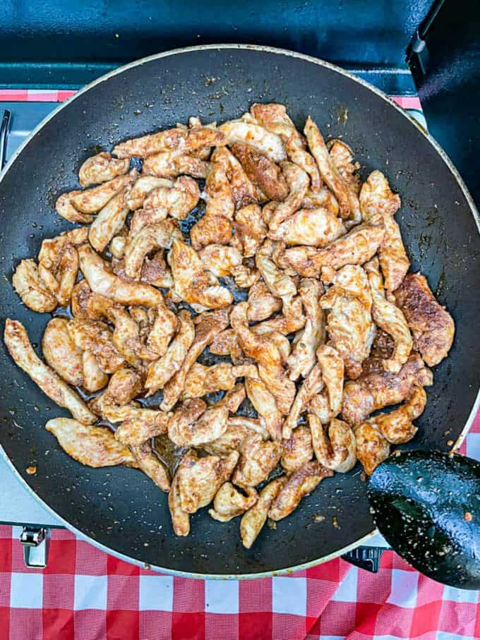 A large skillet with cooked pieces of fajita chicken on a camp stove.