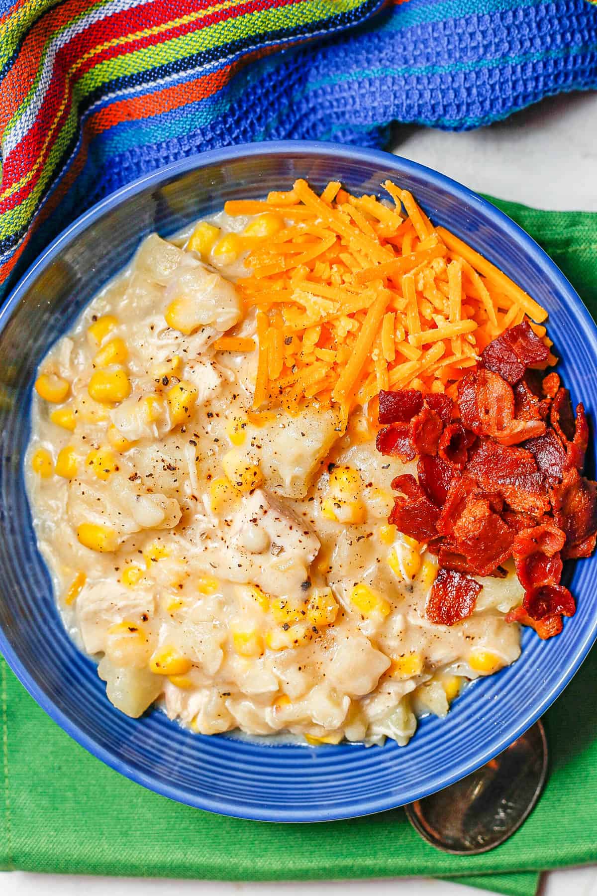 A serving of chicken corn chowder in a blue bowl with cheddar cheese and cooked, crumbled bacon on top.