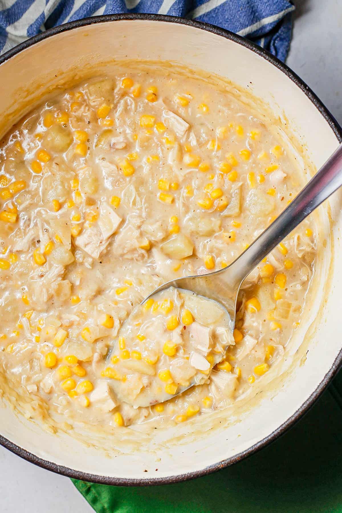 A serving spoon resting in a large deep pot of chicken corn chowder.