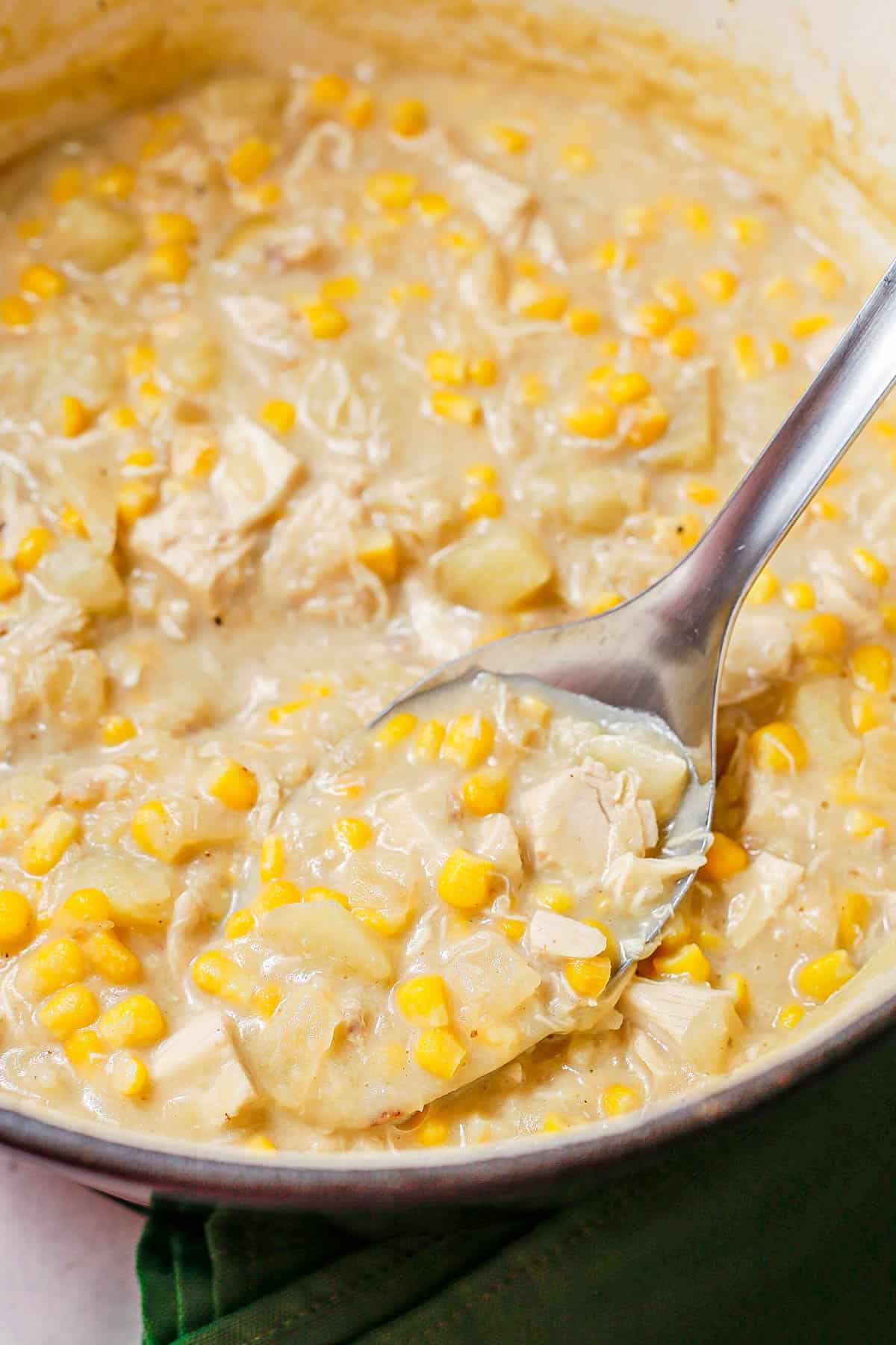 A spoonful of chicken corn chowder being taken from a large deep pot of chowder.
