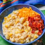 A blue bowl full of chicken corn chowder with cheddar cheese and bacon on top and a text overlay on the photo.