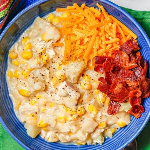 Close up of a serving of chicken corn chowder in a blue bowl with cheddar cheese and cooked, crumbled bacon on top.