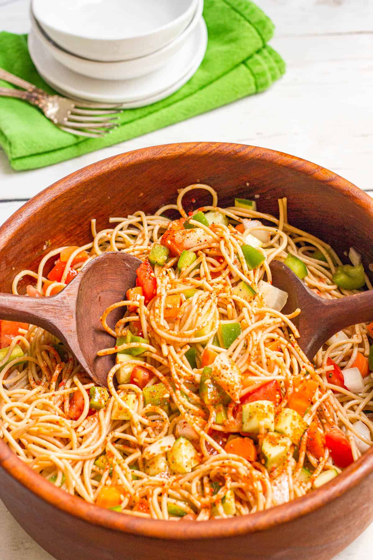 Two wooden salad spoons mixing together a spaghetti pasta salad.