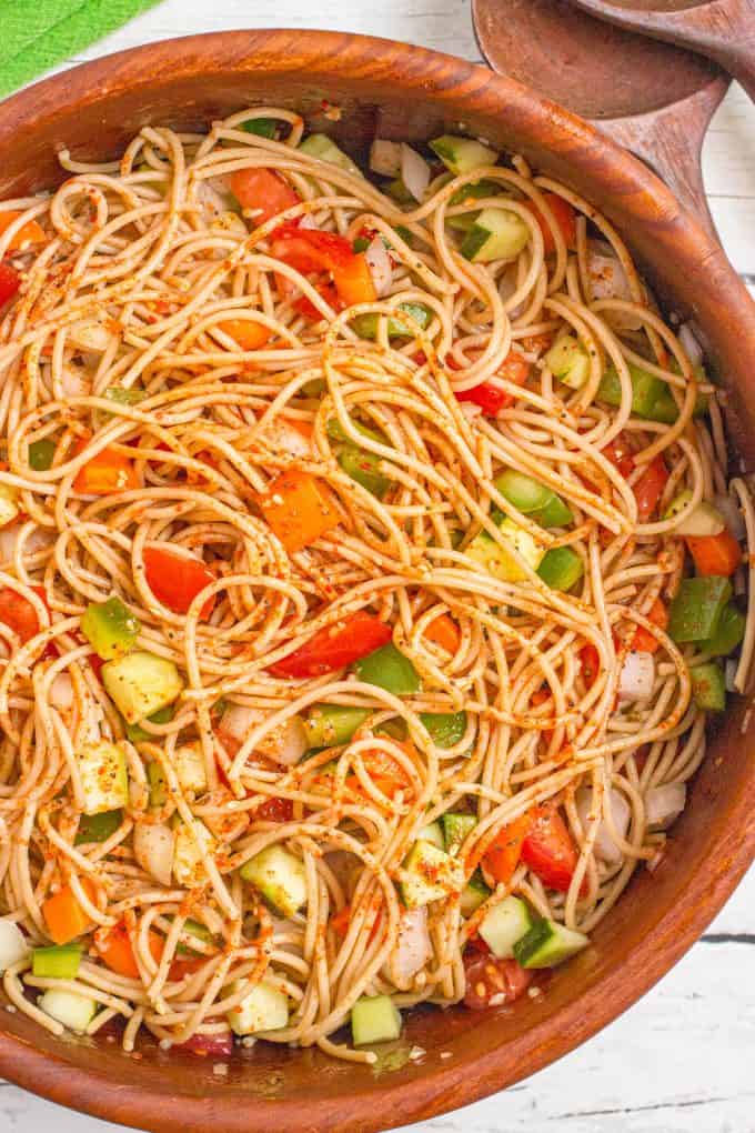 Close up of spaghetti salad with tomatoes, carrots, green peppers and cucumber with Italian dressing and salad seasoning.