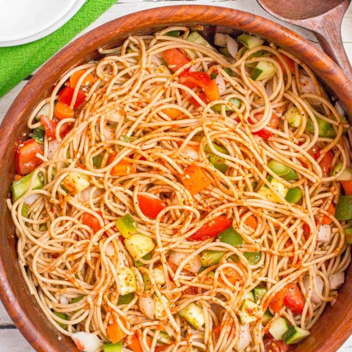 A wooden bowl filled with a pasta salad with spaghetti and fresh veggies.