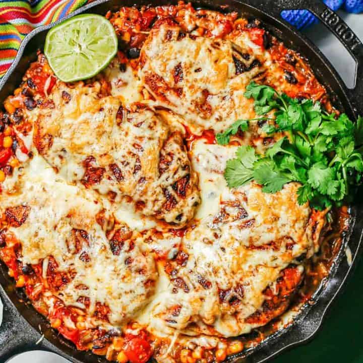 A cast iron skillet with cowboy chicken topped with melted cheese with sprigs of cilantro to the side.